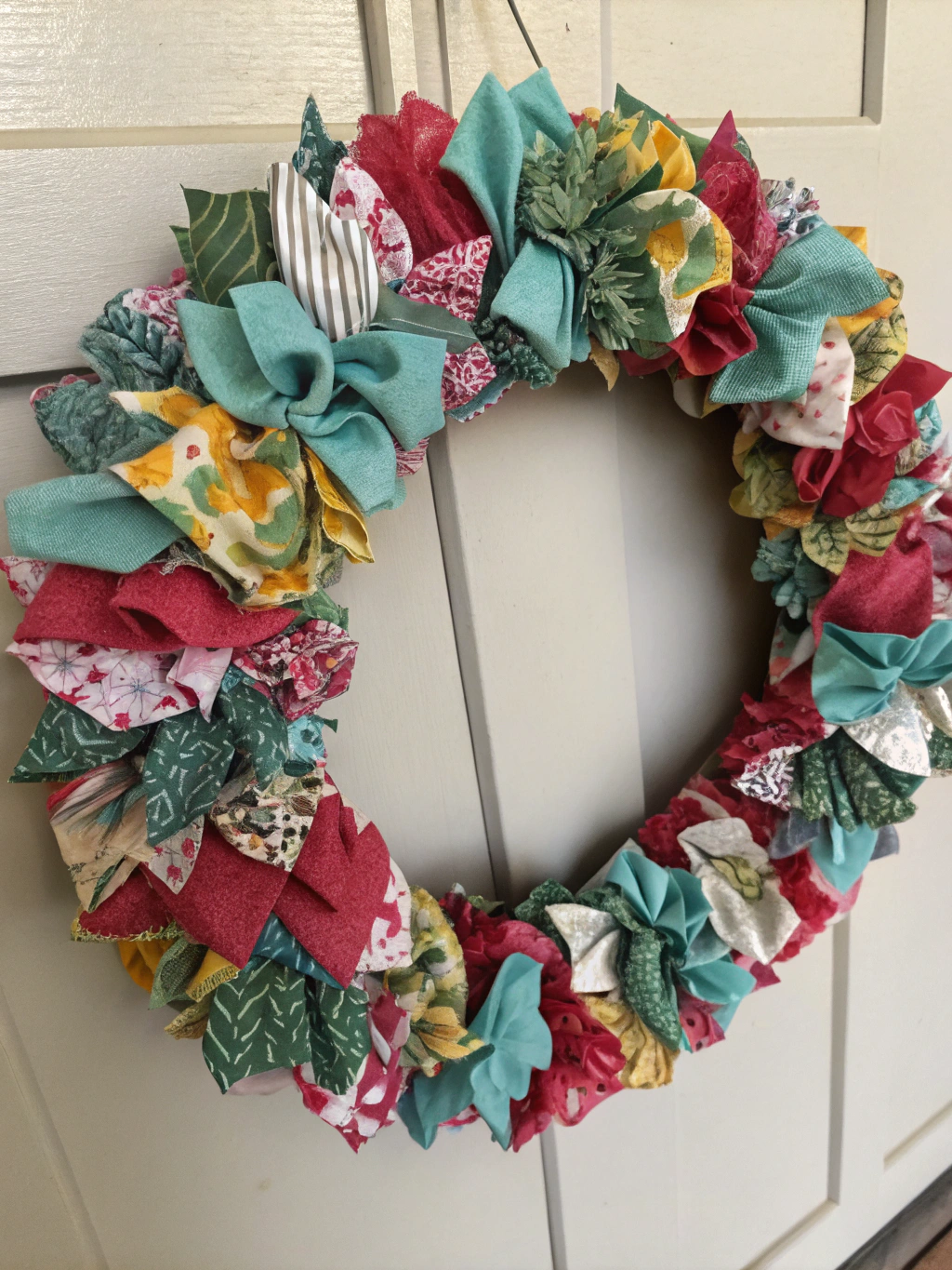 A beautifully finished upcycled fabric scraps wreath hanging on a door, showcasing a variety of colors and textures.